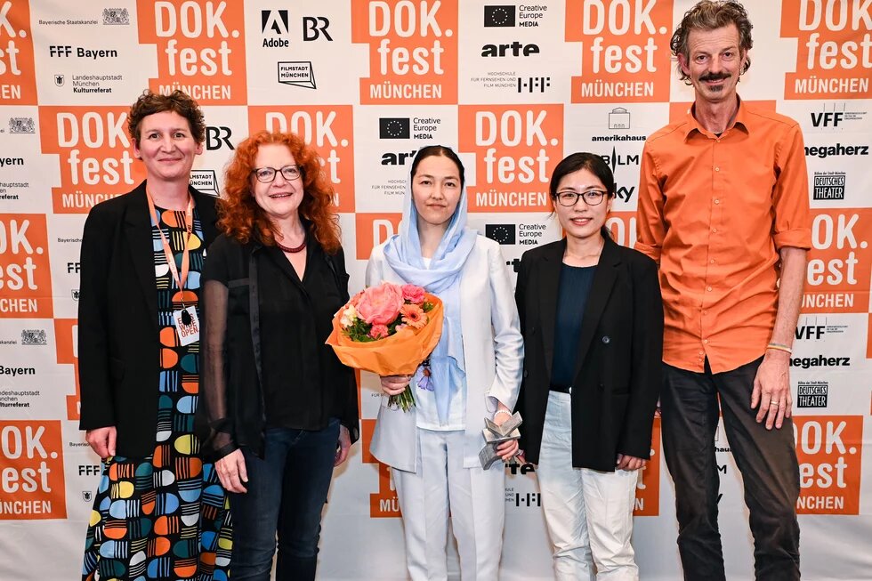 DOK.fest Preisverleihung 2024 mit Menschen vor der DOK.fest Wand